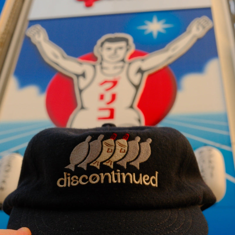 Black discontinued cap held up in front of the Glico running man sign